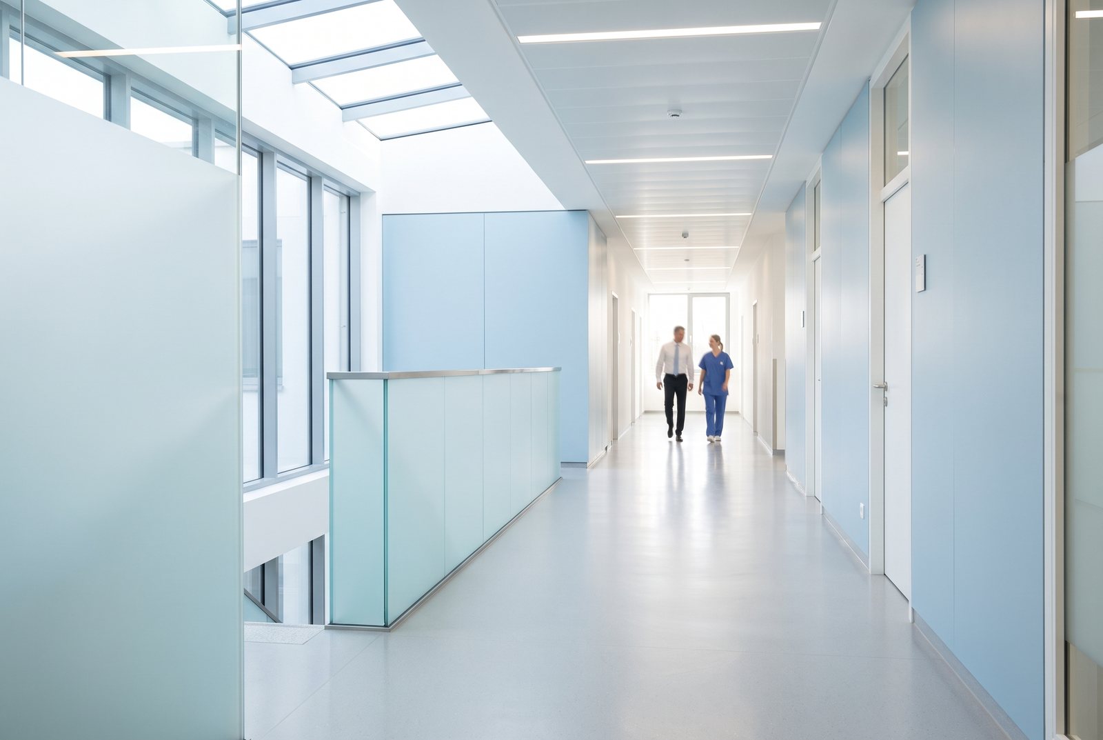 Heller Krankenhausflur mit Glastüren, im Hintergrund zwei Personen